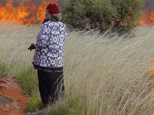 A woman standing in a burning grassland.