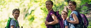 A woman and her three children, all with backpacks, smiling at the camera while hiking in the woods.