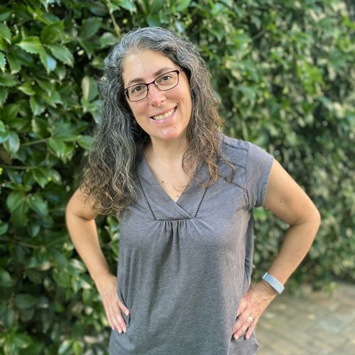 Headshot of Virginia Associate State Director Nikki Rovner. A woman with dark curly hair poses standing in front of a leaf-covered wall.