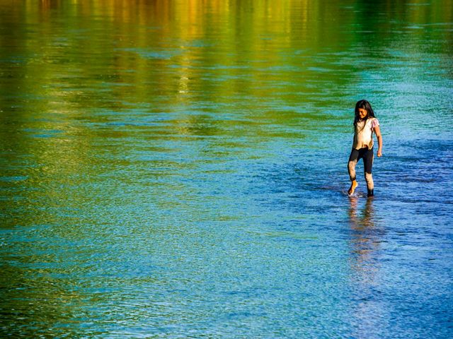 A smiling girl walks slowly with her bare feet in a river at sunset.