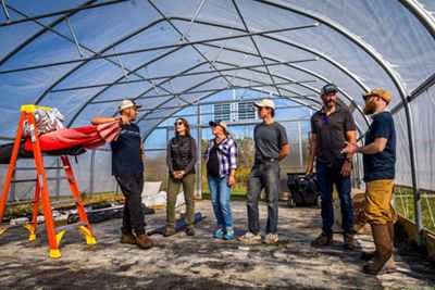 People working inside a greenhouse preparing planting areas.