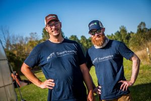 Two people wearing Swiftwater shirts standing in a grassy field.