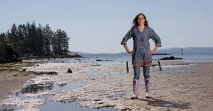 A woman in rubber boots stands on an Alaskan beach at low tide.