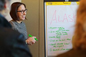 A woman smiling with a green pen in front of a flip chart.