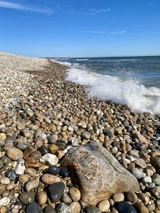 Small waves crash on a steeply sloped beachfront, covered with rounded stones.