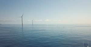 small boat on still sea with offshore wind turbines in distance.