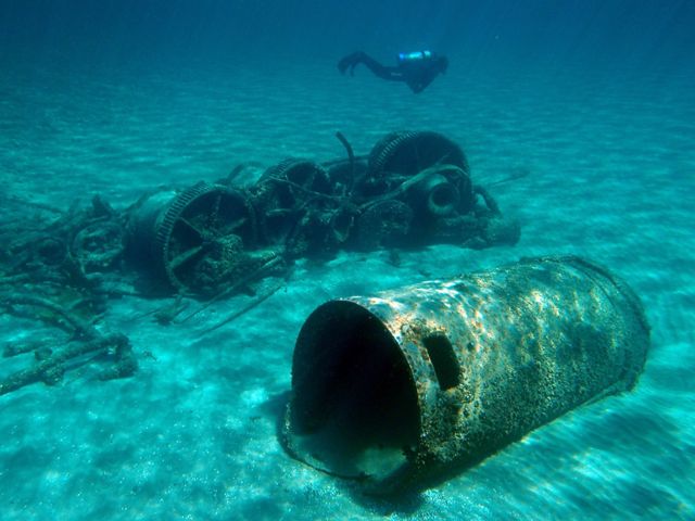 A diver swims through the clear water of Lake Huron. On the lake bottom is iron deck machinery from the wreckage of a working barge.