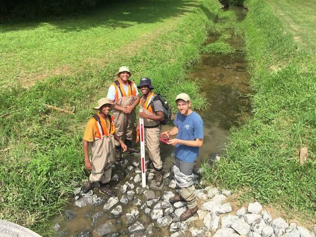 Four interns standing in a rocky culvert wearing waders and smiling up at the camera.
