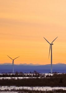 Two wind turbines set against hillside and orange sky.