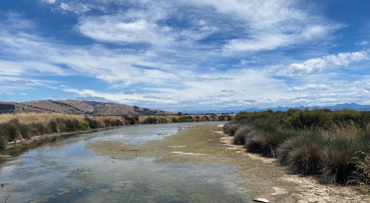 Landscape view of a wide riverbed with some water in it under a blue sky.