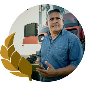 A farmer stands with a tablet in front of equipment.