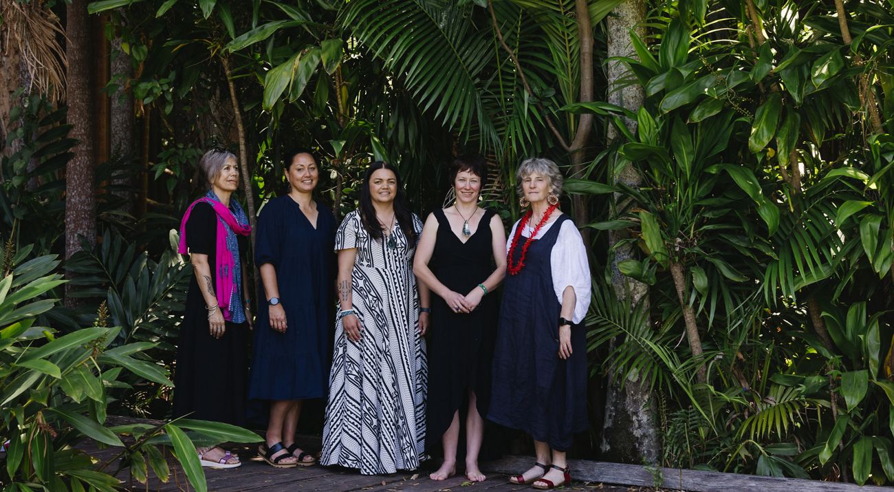 Five women stand together in front of a stand of trees.