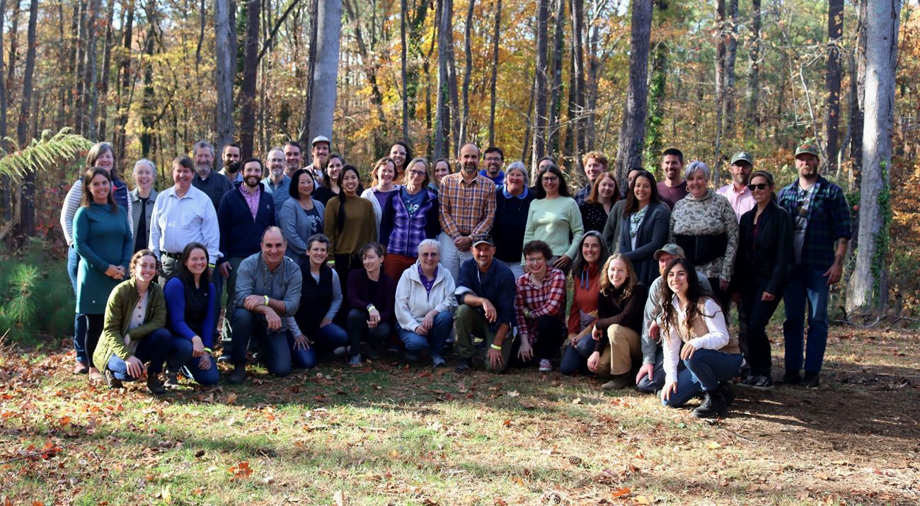A group picture of all the North Carolina staff members. The group is standing in front of trees that have fall-like colors.