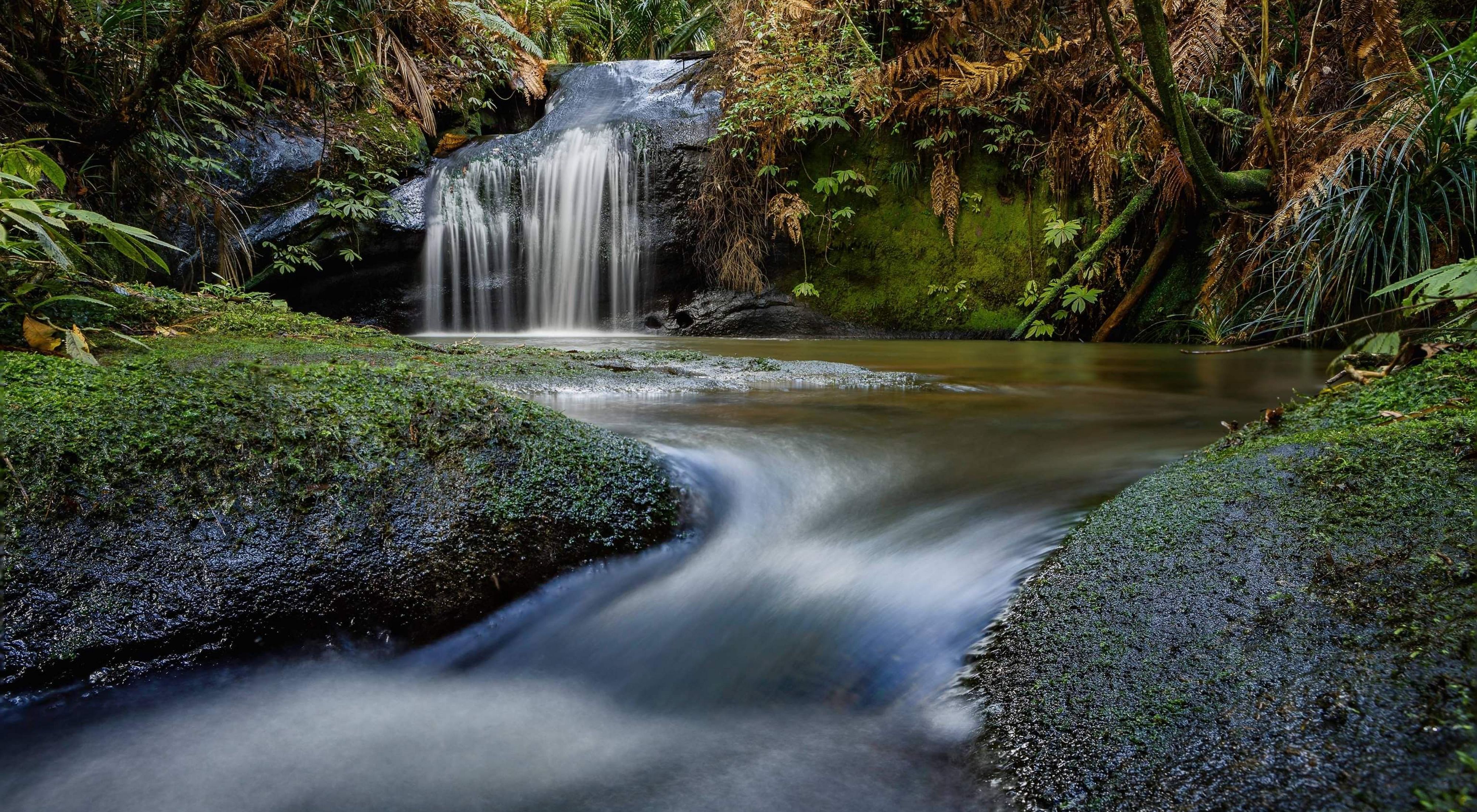 a long exposure photo of a small waterfall and a creek.