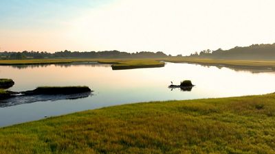 A wide tidal creek winds through green and gold salt marsh grasses on a late summer evening.