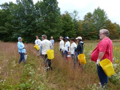 A group of people holding yellow buckets while standing in a grassy field.