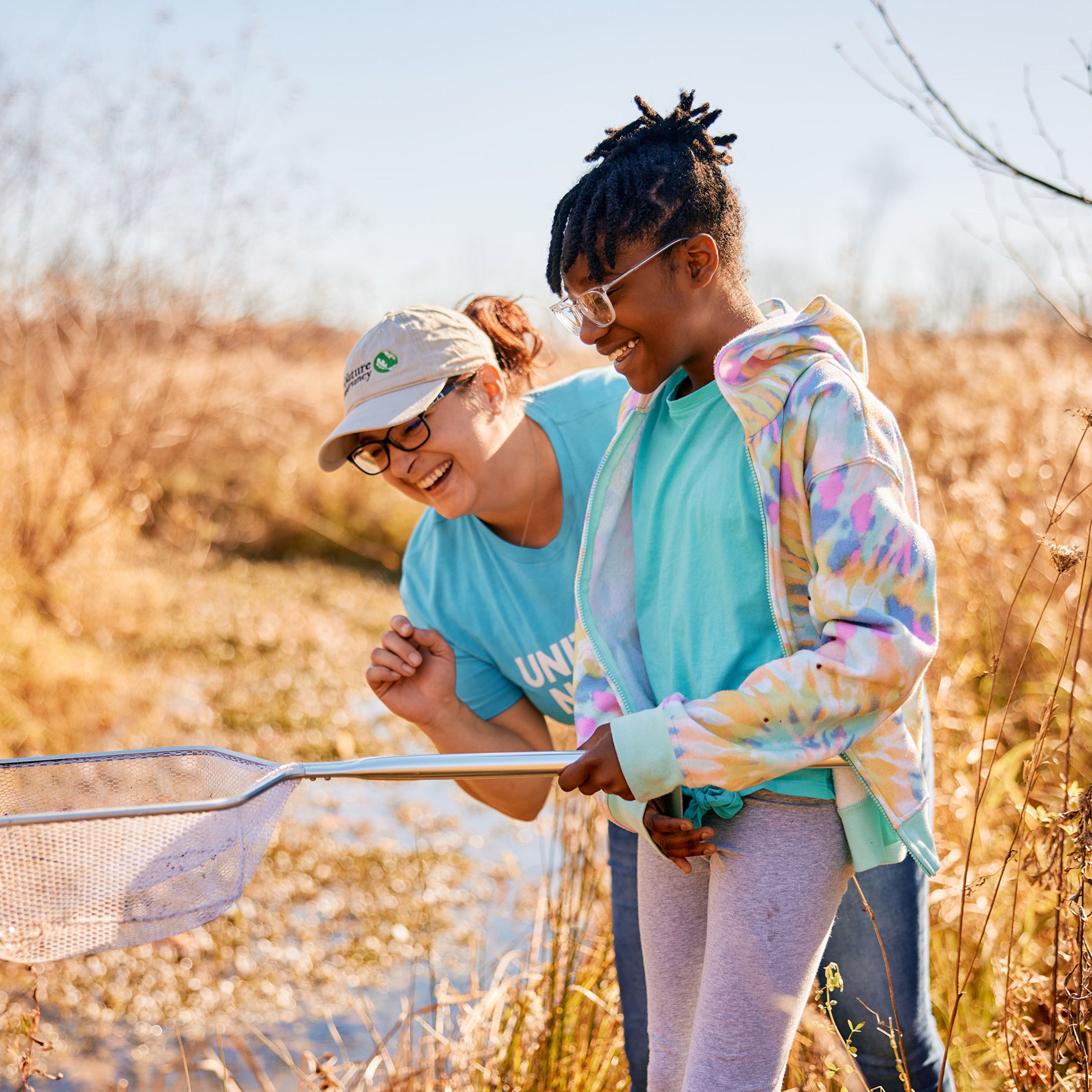 Angie Burke, community and conservation specialist for TNC OhIo, laughs as a girl holds a dip net over a small stream in a field.