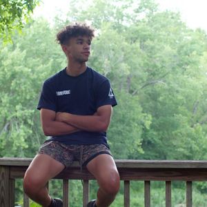 Teen boy sits on wooden railing and looks into distance