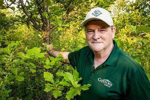 Portrait of David Funk holding tree trunk in his forest.