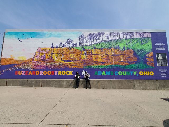 Two Groundwork ORV Green Team members stand in front of large Buzzardroost Rock mural.