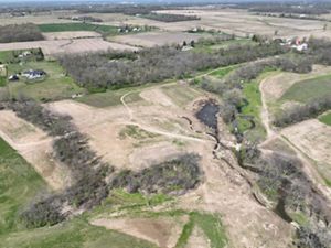 Aerial view of newly constructed stream bed winding through patches of forest.