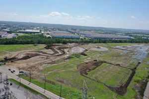 Aerial view of newly dug stream beds in field nestled amongst industrial site.