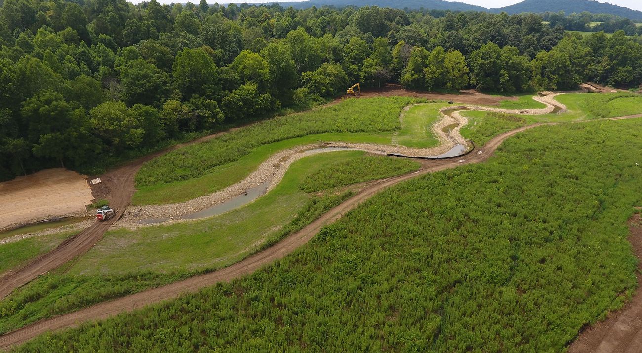 Aerial view of construction equipment and crews helping restore Strait Creek, which winds through a grassy landscape.