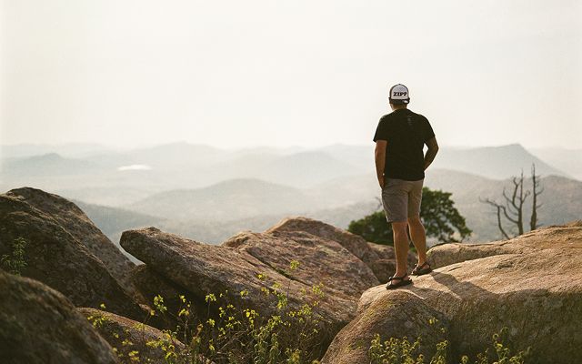 Man standing on mountain rocks overlooking the valley.