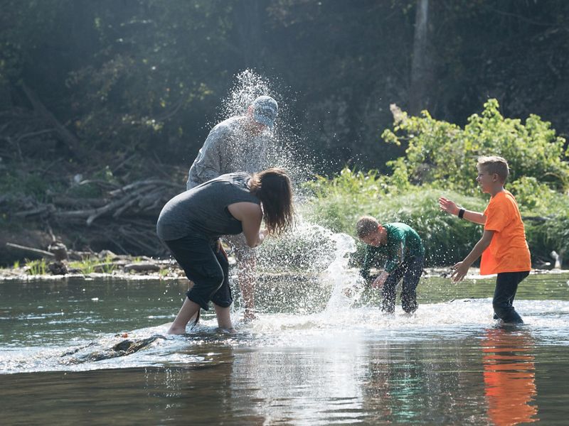 Two adults and two children standing in a river and playfully splashing each other.