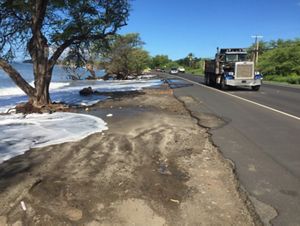 Ocean floodwaters encroach on a road that a tractor-trailer truck is driving down.