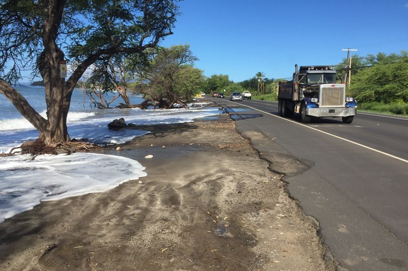 Ocean floodwaters encroach on a road that a tractor-trailer truck is driving down.