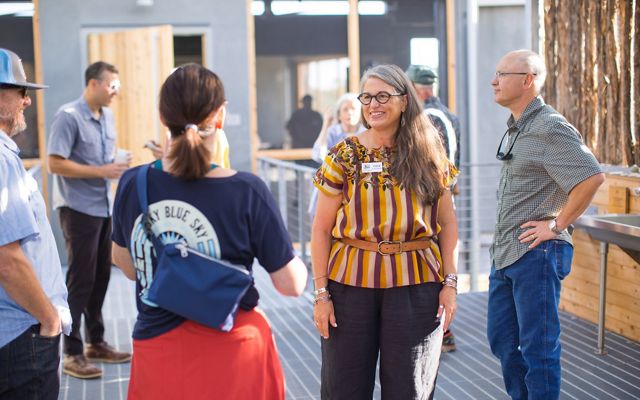 A group of men and women stand together talking in a building.