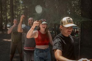 Several people stand in a line and hold up drinking cups and laugh.