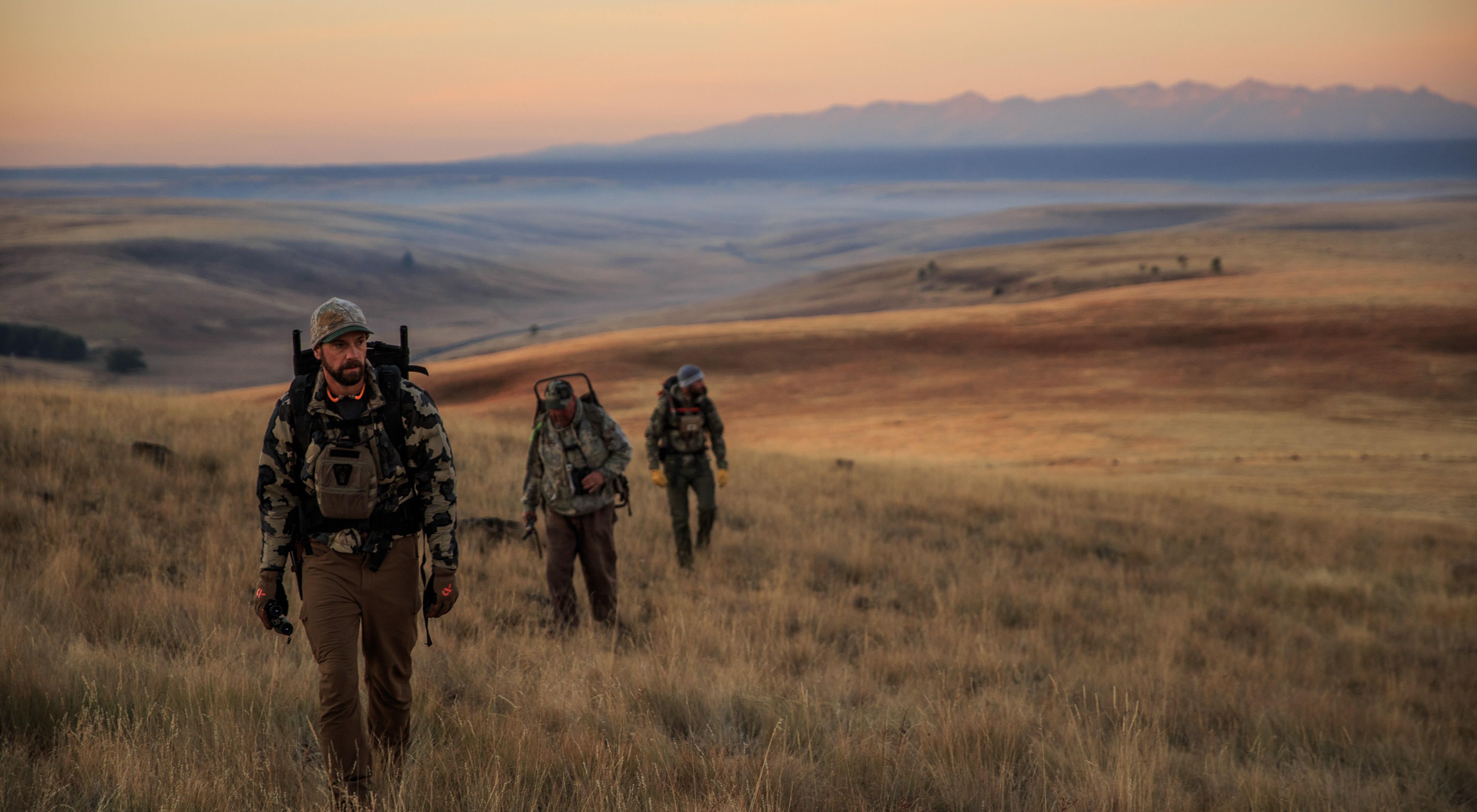 Hunters dressed in camouflage hike across a golden prairie at sunrise at Zumwalt Prairie Preserve.