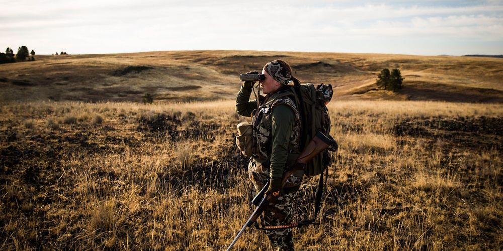 A hunter stands looking through her binoculars during an elk hunt at Zumwalt Prairie Preserve.