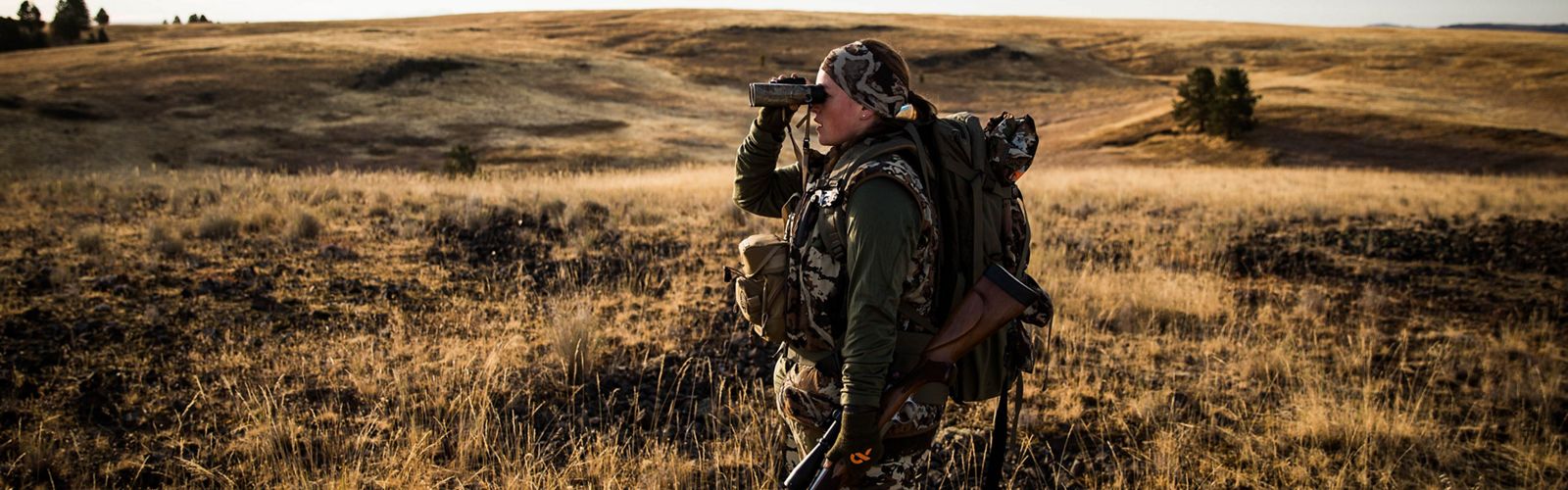 A hunter stands looking through her binoculars during an elk hunt at Zumwalt Prairie Preserve.