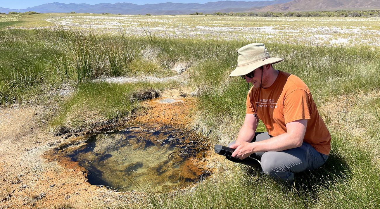 A man kneeling down next to a water hole.