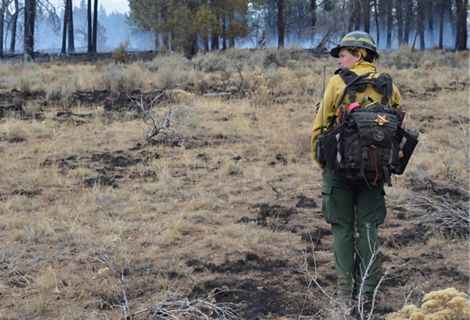 TNC Oregon Fire Manager Katie Sauerbrey stands in fire practitioner gear in front of a forest