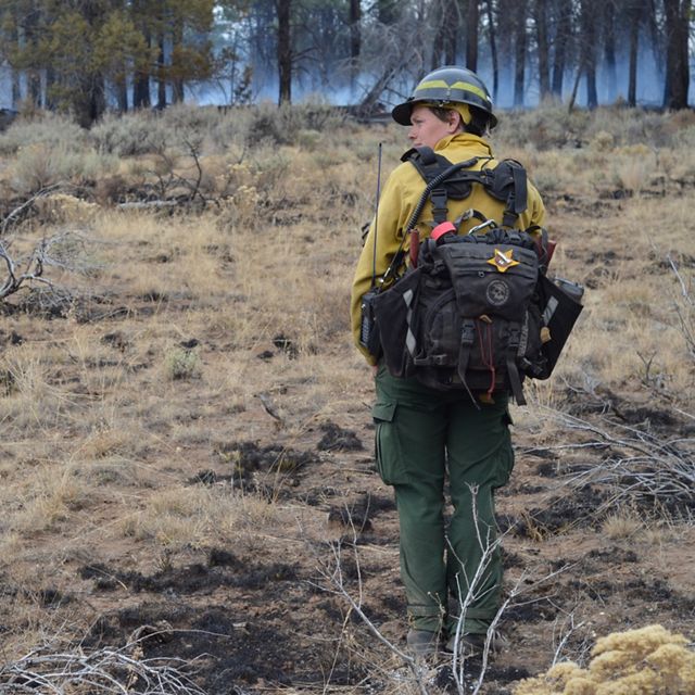 TNC Oregon Fire Manager Katie Sauerbrey stands in fire practitioner gear in front of a forest