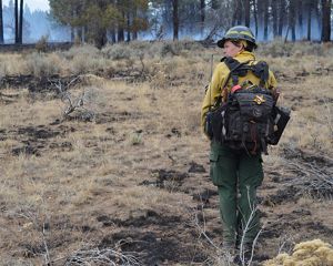 TNC Oregon Fire Manager Katie Sauerbrey stands in fire practitioner gear in front of a forest