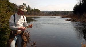 A man stands on the edge of a wooded river.
