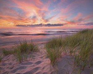 The sun sets over the water and a sandy beach.