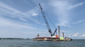 A tall crane on a floating barge is used to move large pieces of crushed granite into place to create new oyster habitat in the Piankatank River.