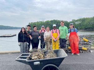 A group of people gathered on a dock with an oyster cage in front of them.