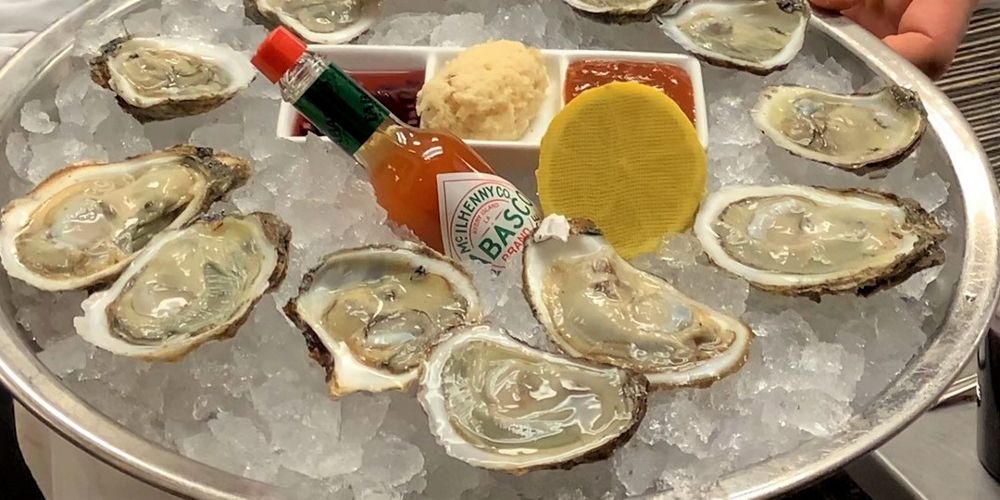 A dozen oysters and a bottle of Tabasco are presented on a silver tray.