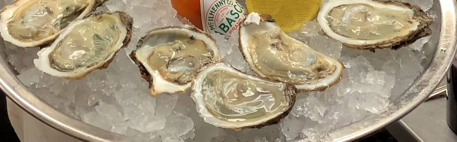 A dozen oysters and a bottle of Tabasco are presented on a silver tray.
