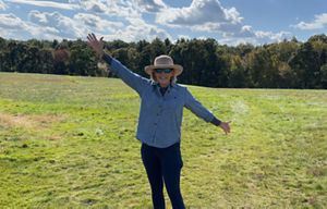 Nancy Gotfredson stands in field with trees in the background.