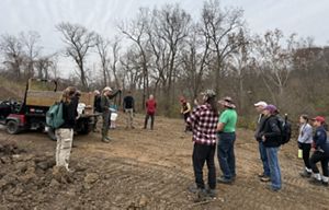 People standing around a circle listening to a woman with a bucket.