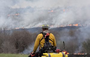 Man on ATV looks into distance of smoke and fire.