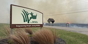 Sign with "The Wilds" text and a prescribed fire and smoke in the background. 